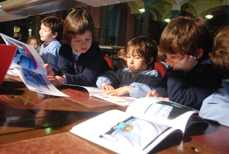 Cuatro niños de jardín manipulando libros impresos, En color.
